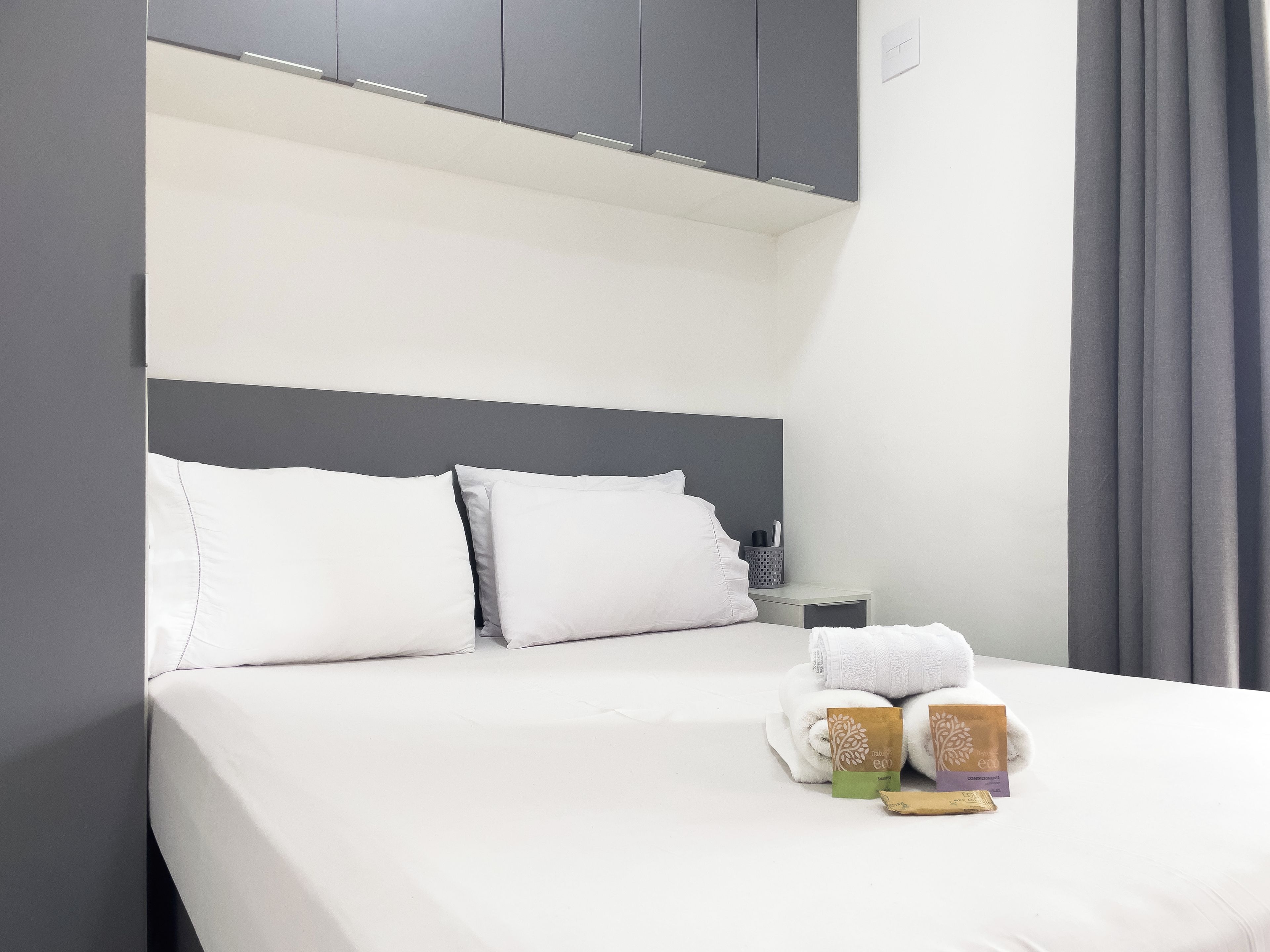 Habitación de hotel con cama, almohadas, mesita de noche y un juego de toallas.