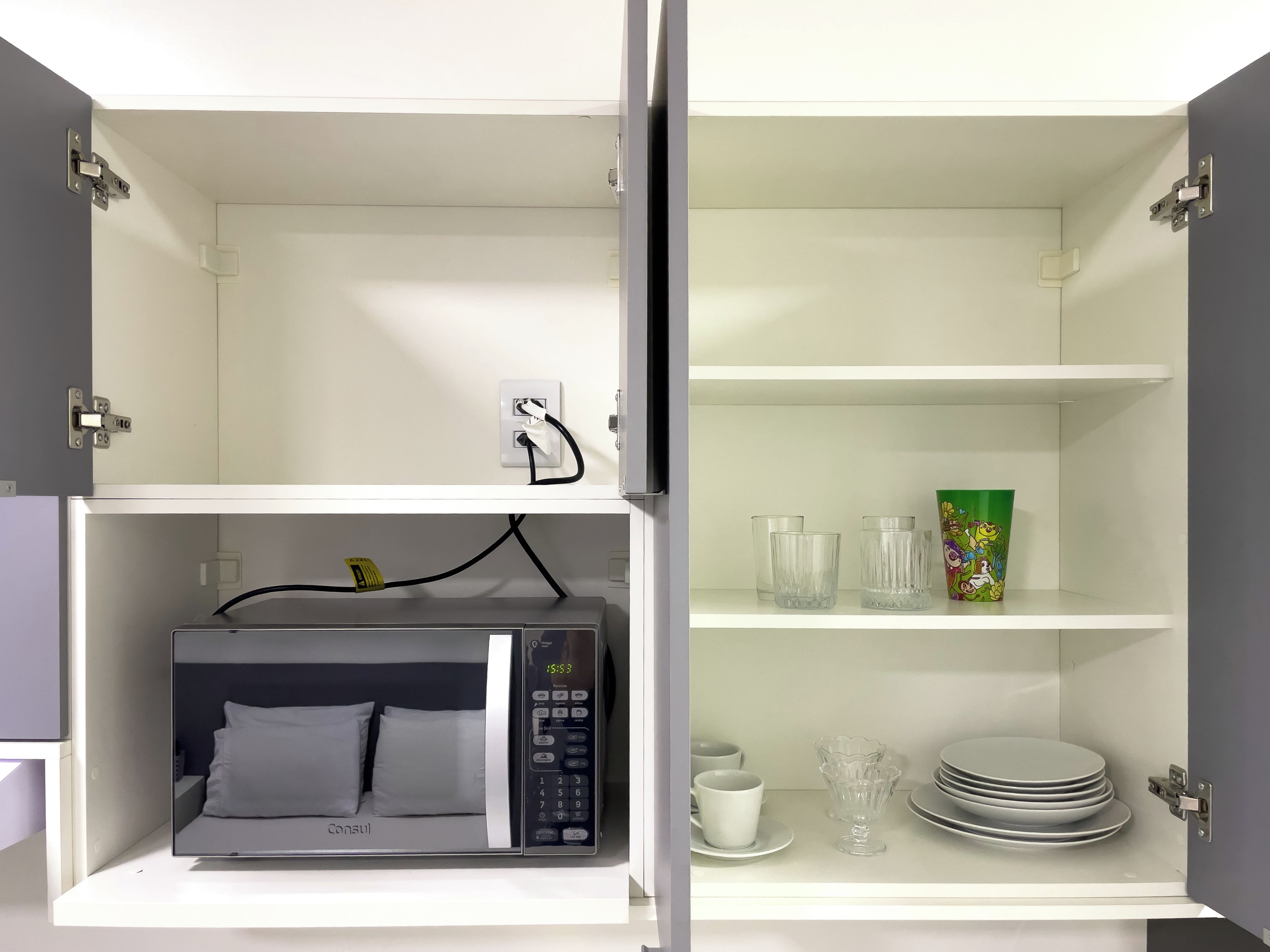 A kitchenette with a microwave, a power outlet, and a shelf with glassware and plates.