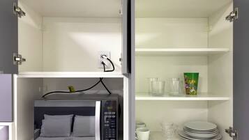 A kitchenette with a microwave, a power outlet, and a shelf with glassware and plates.