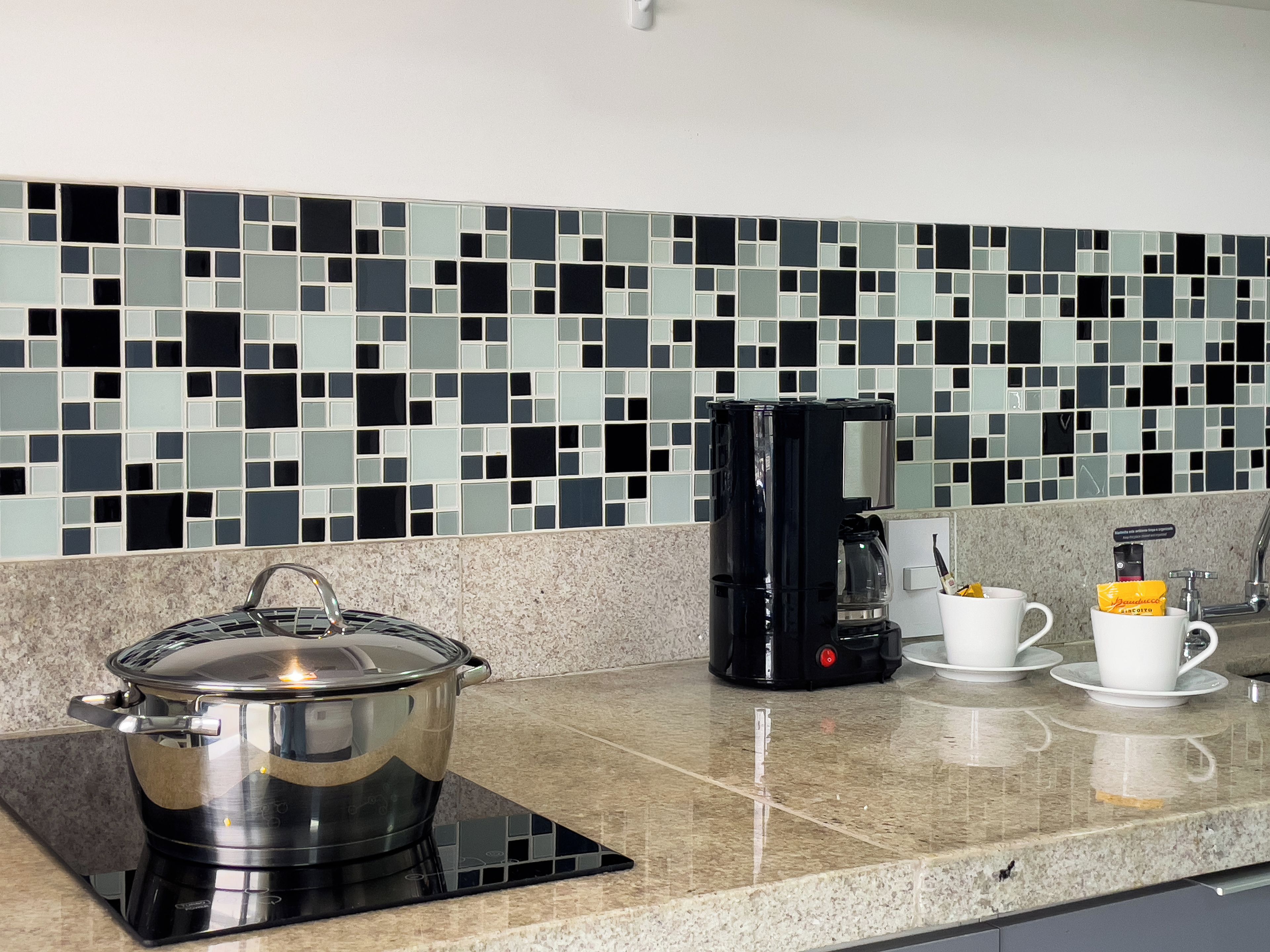 A kitchen with a modern design, featuring a black electric stove, a coffee maker, and a pot on a induction cooktop.