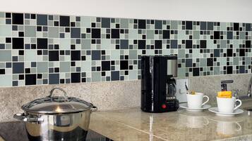 A kitchen with a modern design, featuring a black electric stove, a coffee maker, and a pot on a induction cooktop.
