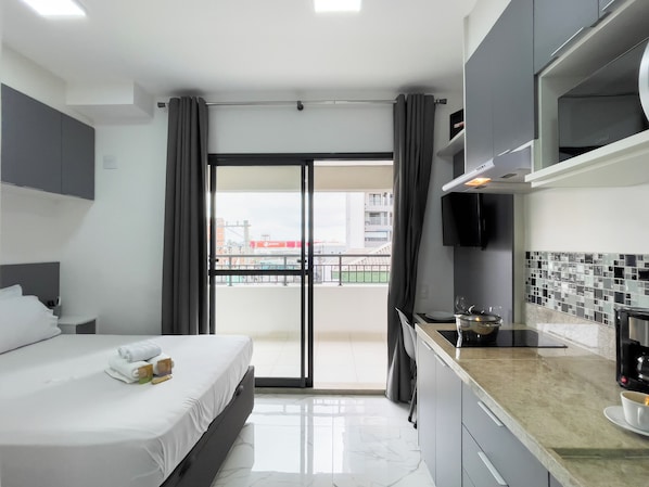 Habitación de hotel con cama, zona de cocina y vistas al exterior.