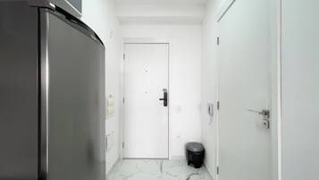 A narrow hallway with a refrigerator on the left, a door at the end, and a trash bin to the right.