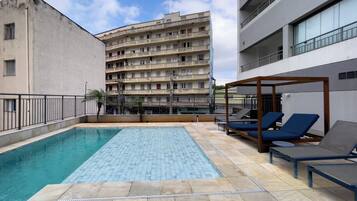 A rooftop pool area with lounge chairs and a building in the background.