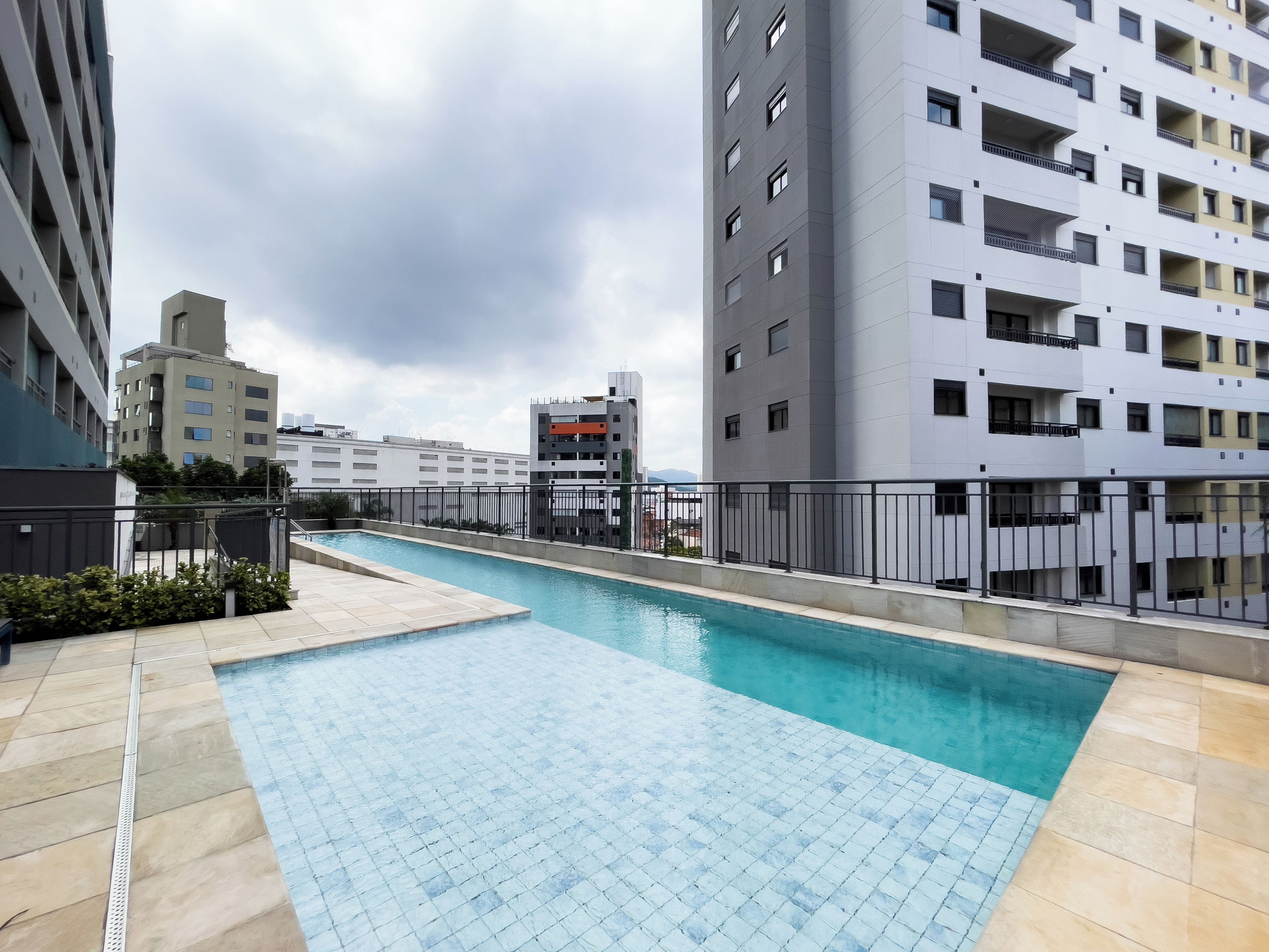 A rooftop swimming pool with a tiled deck, surrounded by high-rise buildings.