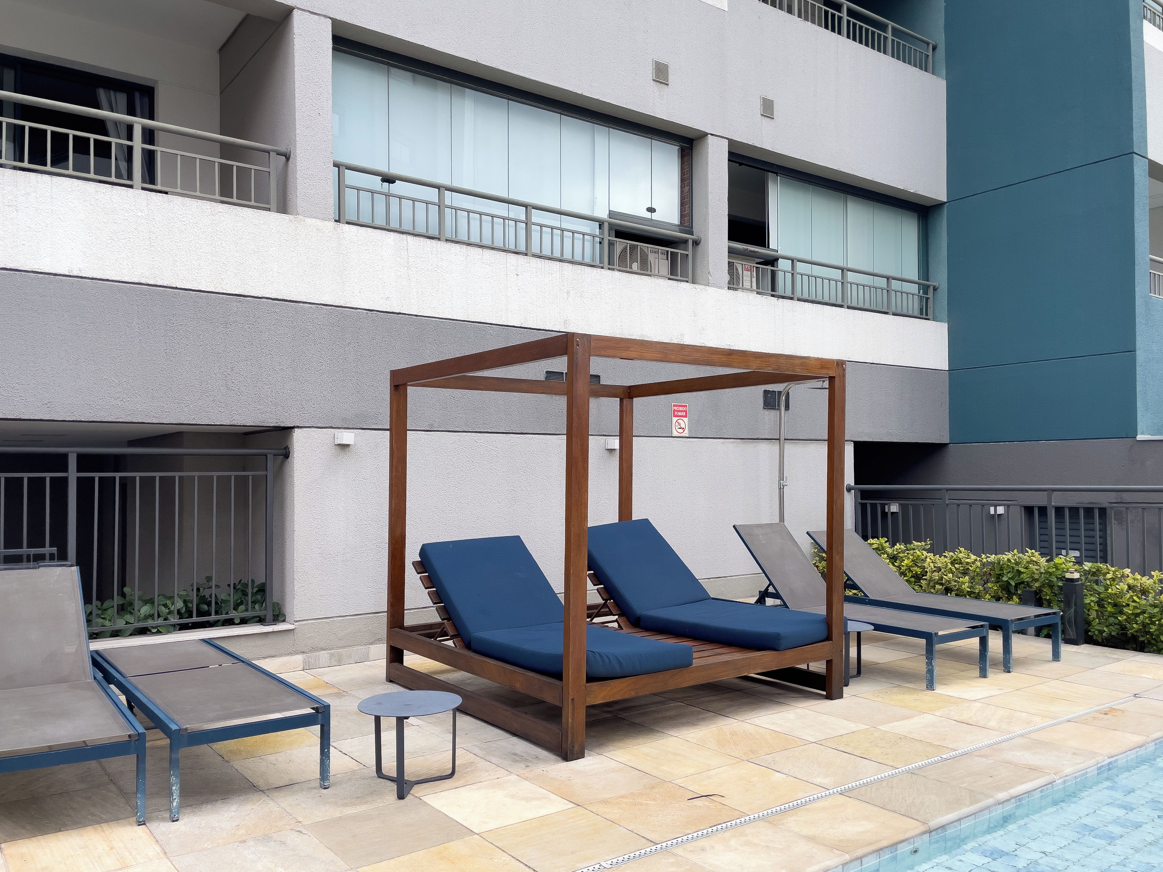 Un espace aménagé au bord de la piscine, doté d’un auvent en bois, de chaises longues et d’une petite table.