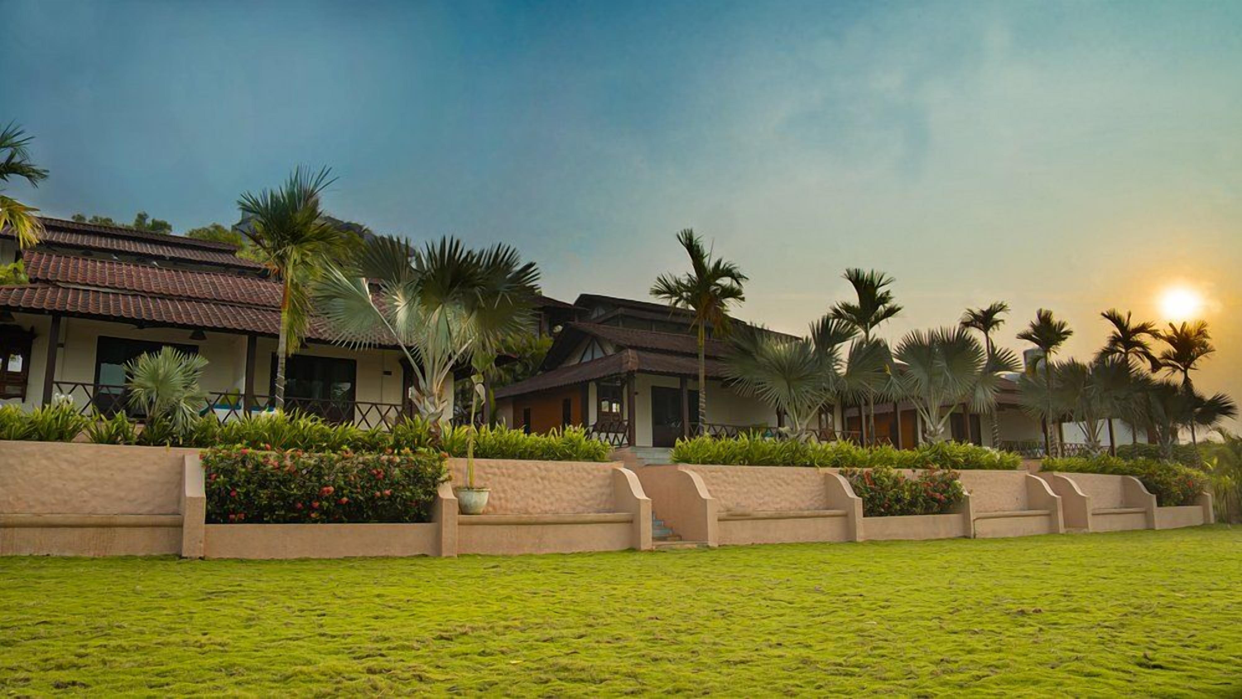 A hotel with a traditional architectural style, featuring a courtyard with palm trees and a well-maintained lawn.