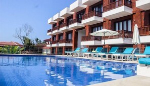 Un hotel con piscina, varios balcones y tumbonas.
