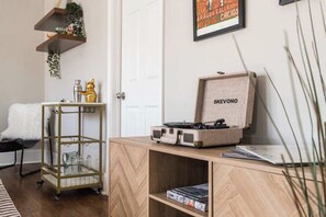 A room with a wooden cabinet, a record player, a metal cart, and a framed picture on the wall. - Artsy Chicago Stay with Patio, Parking & Sleeps 7 (Chicago)