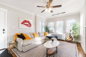 A living room with a sectional sofa, a round coffee table, a ceiling fan, and a guitar. - Artsy Chicago Stay with Patio, Parking & Sleeps 7 (Chicago)