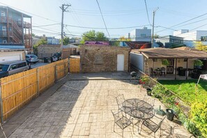 A backyard with a brick patio, a metal table and chairs, a wooden fence, and a small brick building. - Artsy Chicago Stay with Patio, Parking & Sleeps 7 (Chicago)