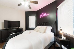 A bedroom with a bed, a television, a ceiling fan, a neon sign, and a bedside lamp. - Artsy Chicago Stay with Patio, Parking & Sleeps 7 (Chicago)