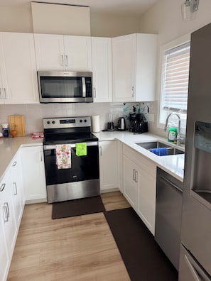A modern kitchen with white cabinets, stainless steel appliances, and a wooden floor. - Ubbies place 1-Entire 4-Bed House - Private - Sleeps 8 - Regina (Regina)