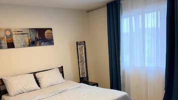 Ein Schlafzimmer mit einem Bett, einem Nachttisch, einem Wandbild und einem Fenster mit Vorhängen.