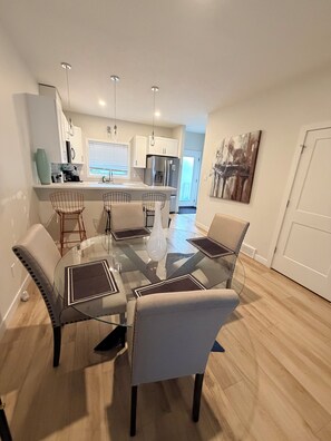 A modern kitchen with white cabinets, stainless steel appliances, and a glass dining table with four chairs. - Ubbies place 1-Entire 4-Bed House - Private - Sleeps 8 - Regina (Regina)