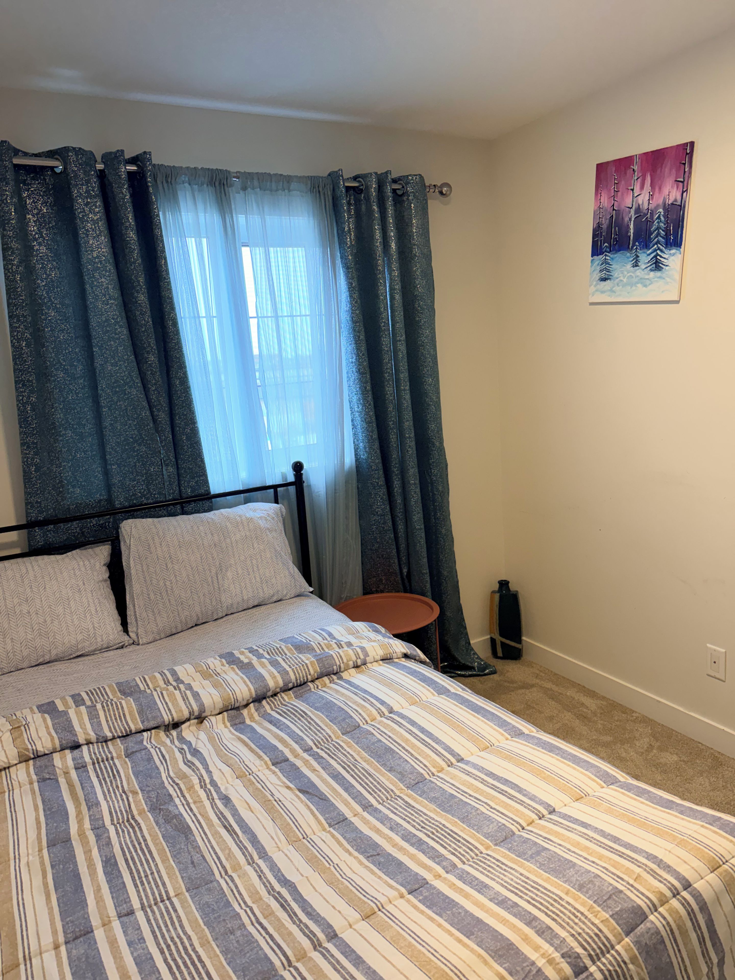 Une chambre à coucher avec un lit, des rideaux, une petite table et un tableau au mur.