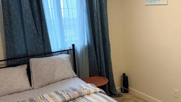 Une chambre à coucher avec un lit, des rideaux, une petite table et un tableau au mur.