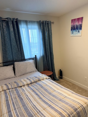 A bedroom with a bed, curtains, a small table, and a wall painting. - Ubbies place 1-Entire 4-Bed House - Private - Sleeps 8 - Regina (Regina)