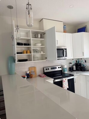 A modern kitchen with white cabinetry, a stainless steel stove, and hanging light fixtures. - Ubbies place 1-Entire 4-Bed House - Private - Sleeps 8 - Regina (Regina)