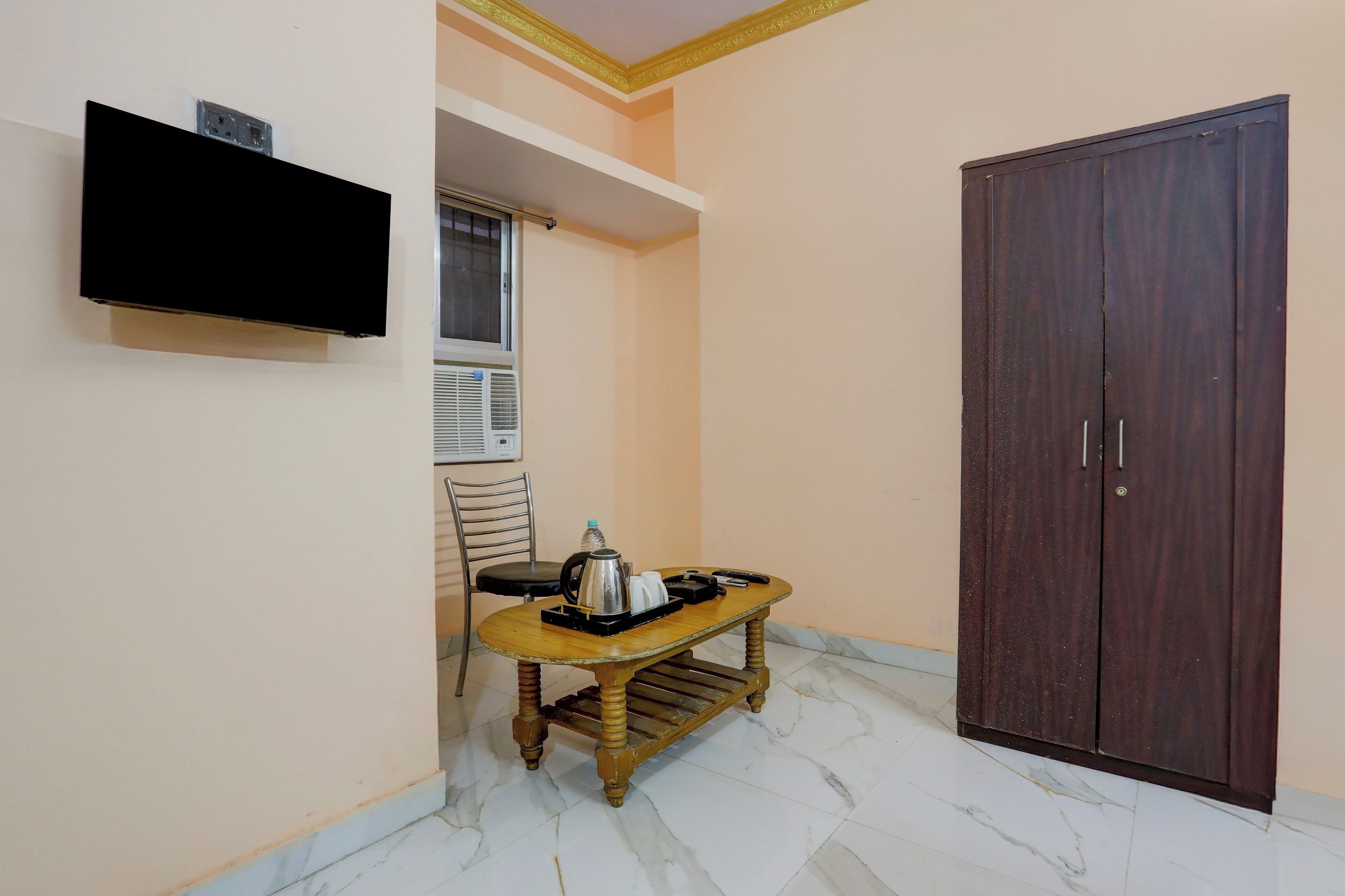 A small room with a wooden table, a chair, a television mounted on the wall, and a wardrobe.