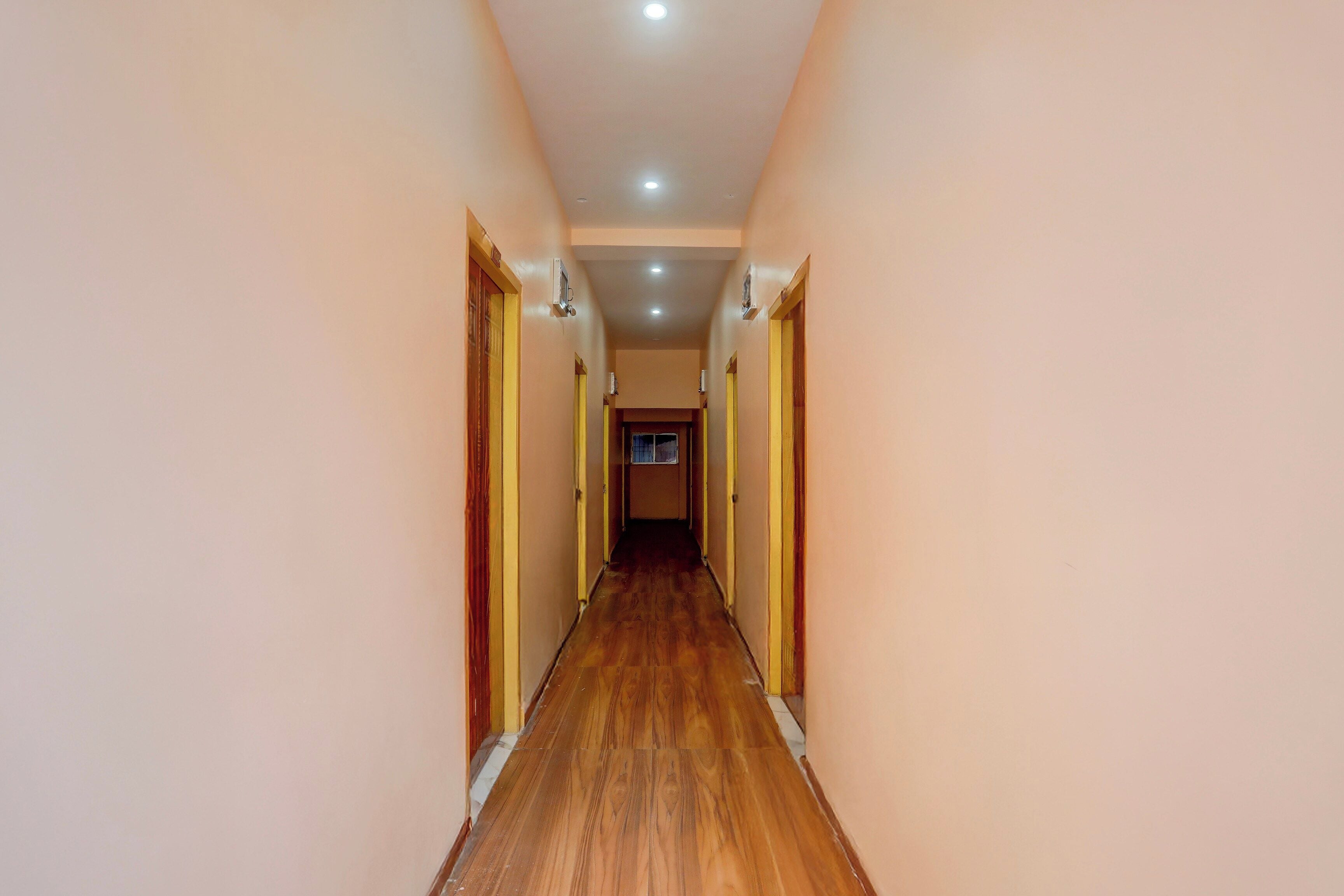 Un pasillo con suelo de madera y paredes color crema, que conduce a una puerta al final.