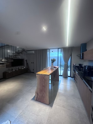A modern kitchen with a central island, a dining area with chairs, and a staircase leading to an upper level. - New Listing (São Miguel dos Milagres)