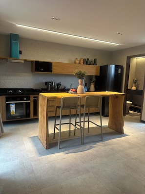 Een moderne keuken met een centraal eiland, barkrukken, een inbouwoven en een koelkast.