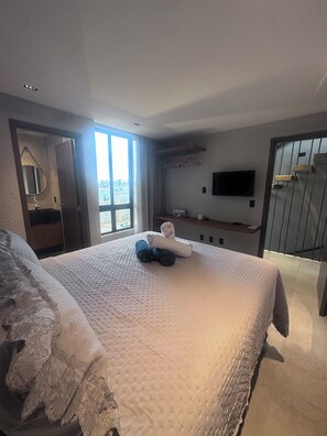 Een hotelkamer met een groot bed, een aan de muur bevestigde televisie en een raam met uitzicht op het omliggende landschap.