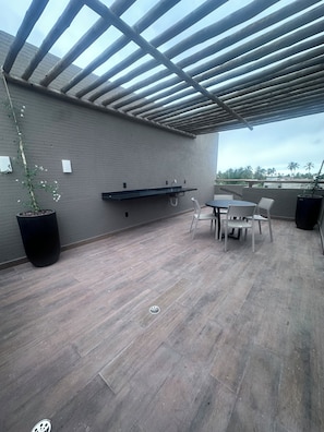 An outdoor patio with a table and chairs, a black planter with a plant, and a grey brick wall. - New Listing (São Miguel dos Milagres)