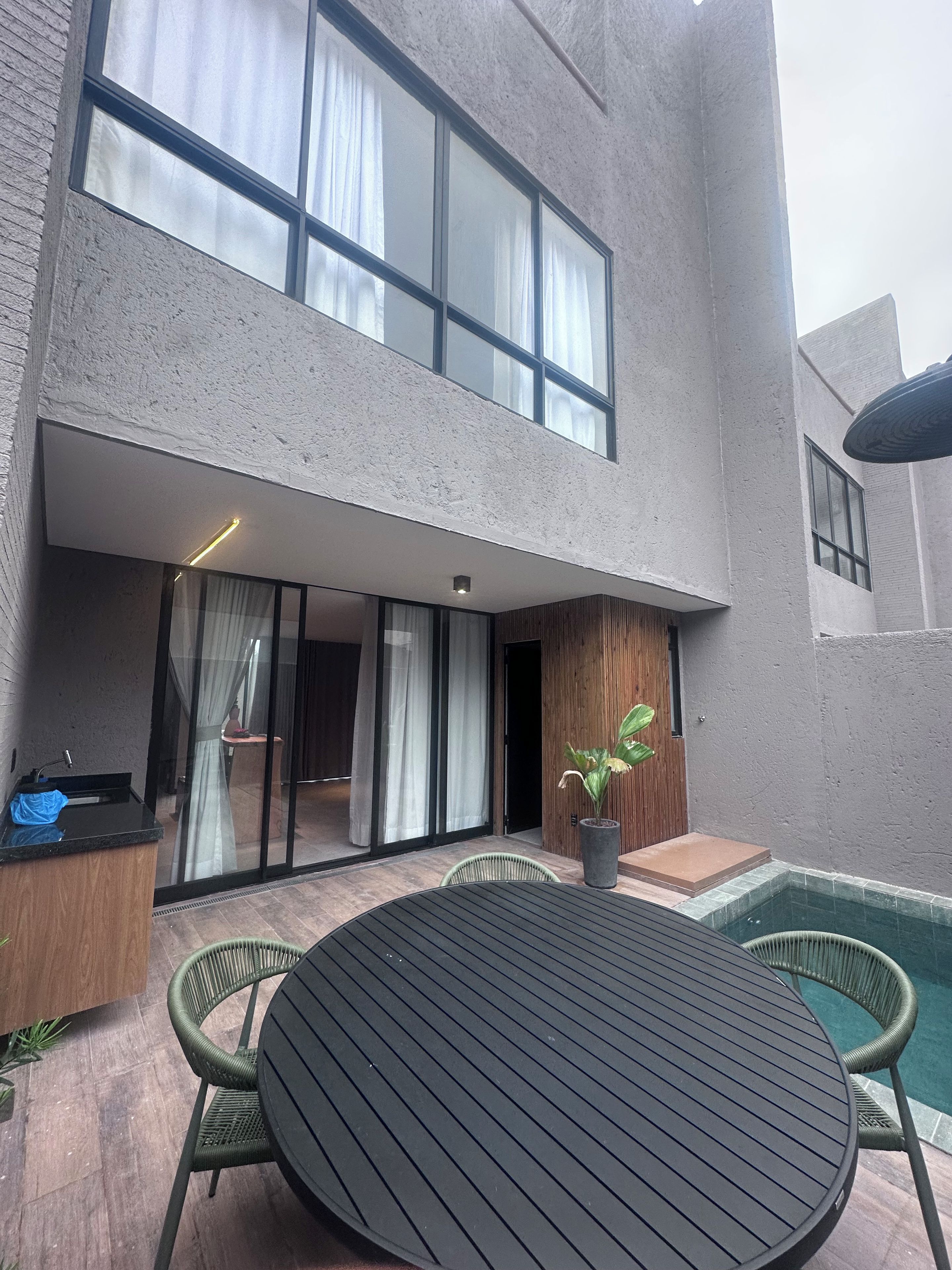 A modern building with a large glass door leading to a covered outdoor area with a pool and seating.