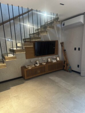 Una escalera de diseño moderno, un televisor de pantalla plana montado en la pared y un mueble de madera con objetos decorativos.