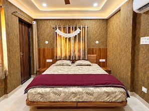 A bedroom with a bed, curtains, a headboard, and a wall-mounted air conditioning unit. - Hotel Utsav (Maheshwar)