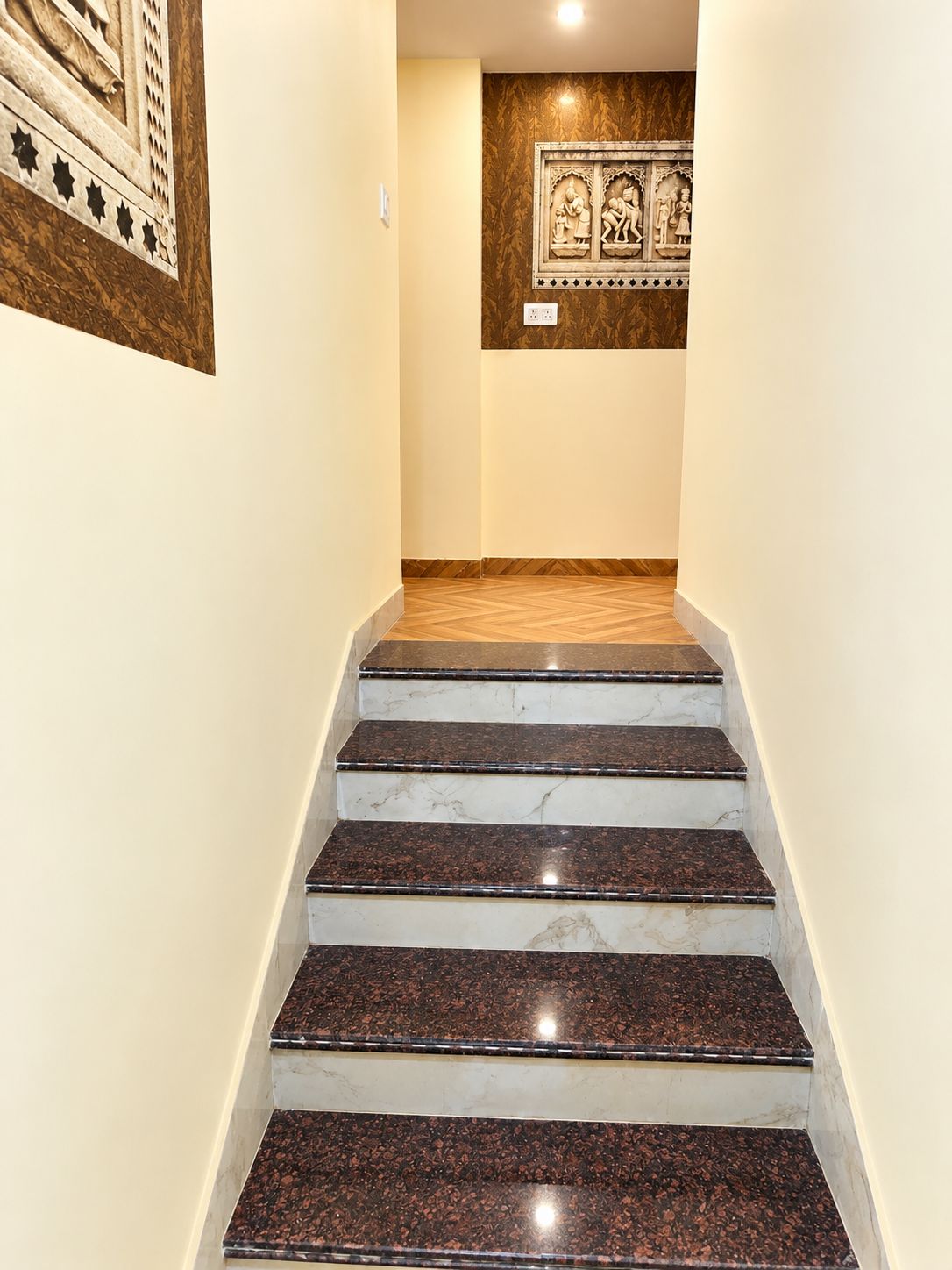 Una escalera con escalones de mármol que conduce a una habitación con un papel tapiz estampado y una obra de arte enmarcada.