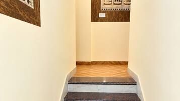 Una escalera con escalones de mármol que conduce a una habitación con un papel tapiz estampado y una obra de arte enmarcada.
