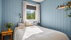 A bedroom with a bed, a nightstand, a window with curtains, and a shelf with plants. - Fabulous 2-bedroom estate in charming Nordland perfect for relaxing getaway (Nordland)