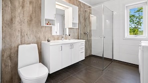A modern bathroom with a toilet, a shower enclosure, a sink with a mirror, and a window with a view of trees. - Fabulous 2-bedroom estate in charming Nordland perfect for relaxing getaway (Nordland)