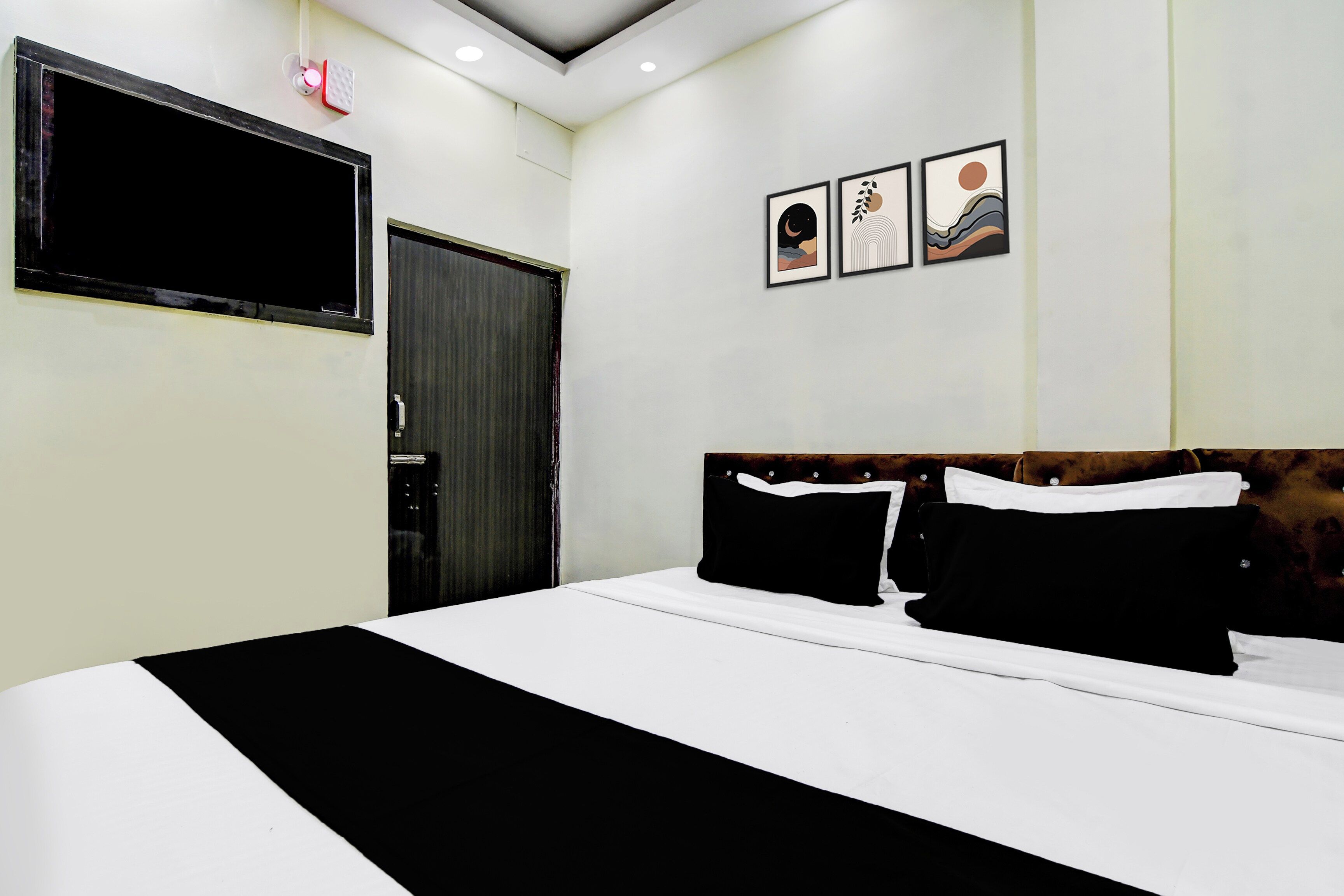 A hotel room with a bed, a flat-screen TV mounted on the wall, and three framed artworks above the bed.