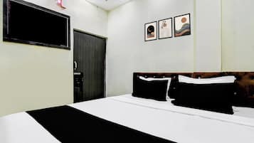 A hotel room with a bed, a flat-screen TV mounted on the wall, and three framed artworks above the bed.