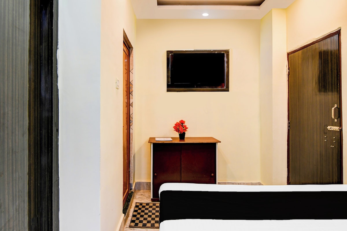 Een hotelkamer met een bed, een klein houten kastje, een aan de muur bevestigde televisie en een deur.