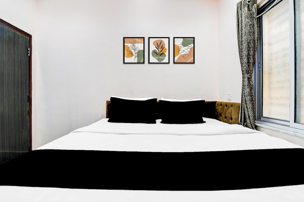 Een hotelkamer met een bed, een raam met gordijnen, en drie ingelijste kunstwerken aan de muur.