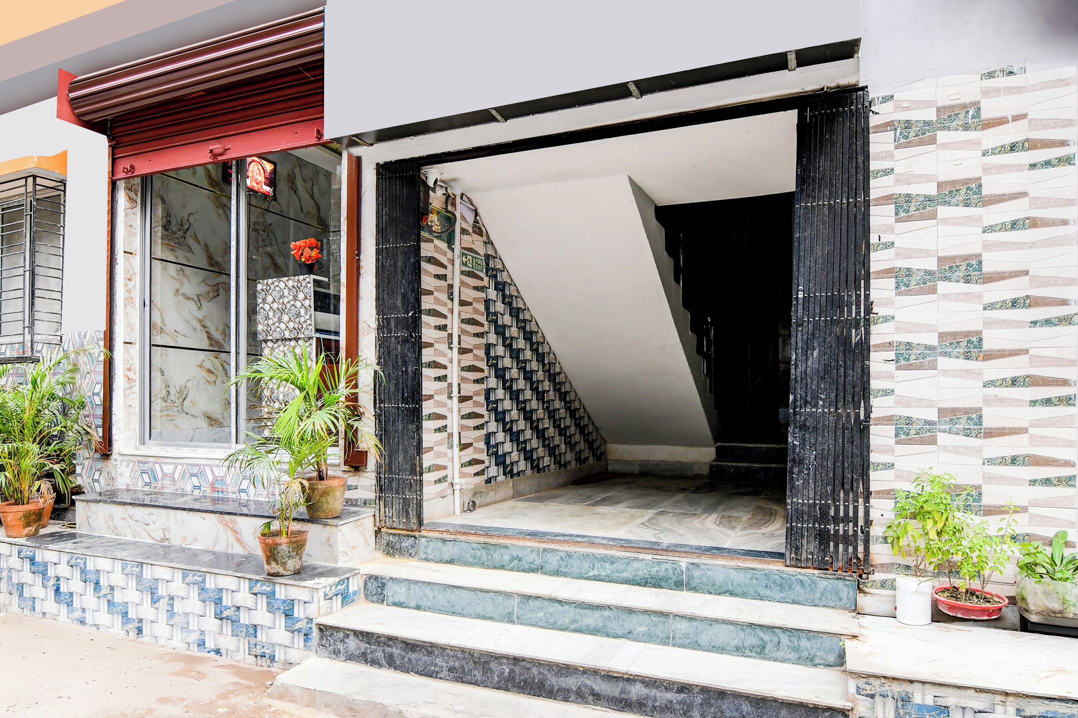 Fachada de un edificio con azulejos, una escalera que conduce a la entrada y plantas en macetas en el suelo.