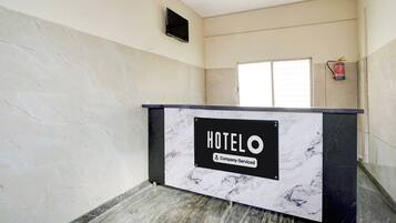 Un mostrador de recepción de hotel con diseño de mármol, un extintor en la pared y una ventana con persianas.