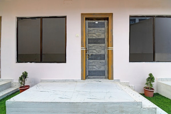 A building facade with a central door, flanked by two large windows, and a small garden area with potted plants. - Townhouse Mandarmani Beach (Kanthi)