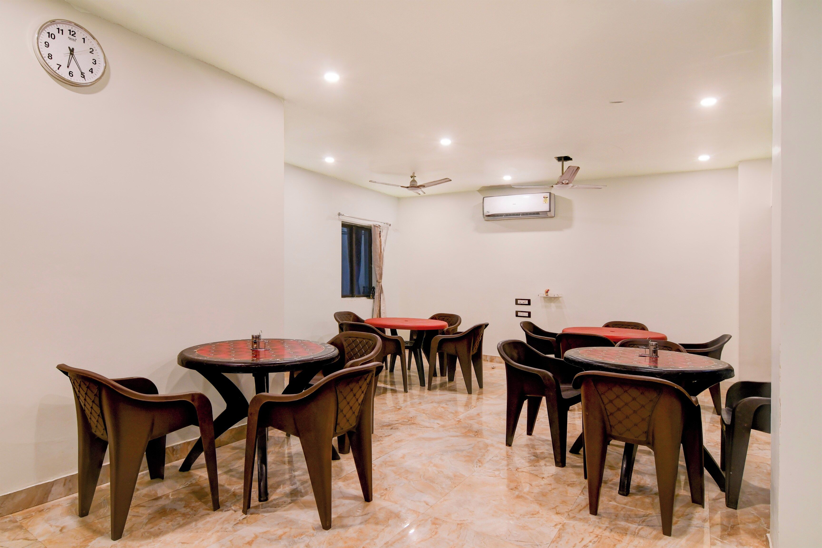Un comedor con varias mesas y sillas, un reloj en la pared y un ventilador de techo.