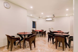 A dining area with multiple tables and chairs, a clock on the wall, and a ceiling fan. - Townhouse Mandarmani Beach (Kanthi)