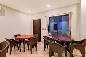 A dining area with two round tables, chairs, a door, and a window with curtains. - Townhouse Mandarmani Beach (Kanthi)