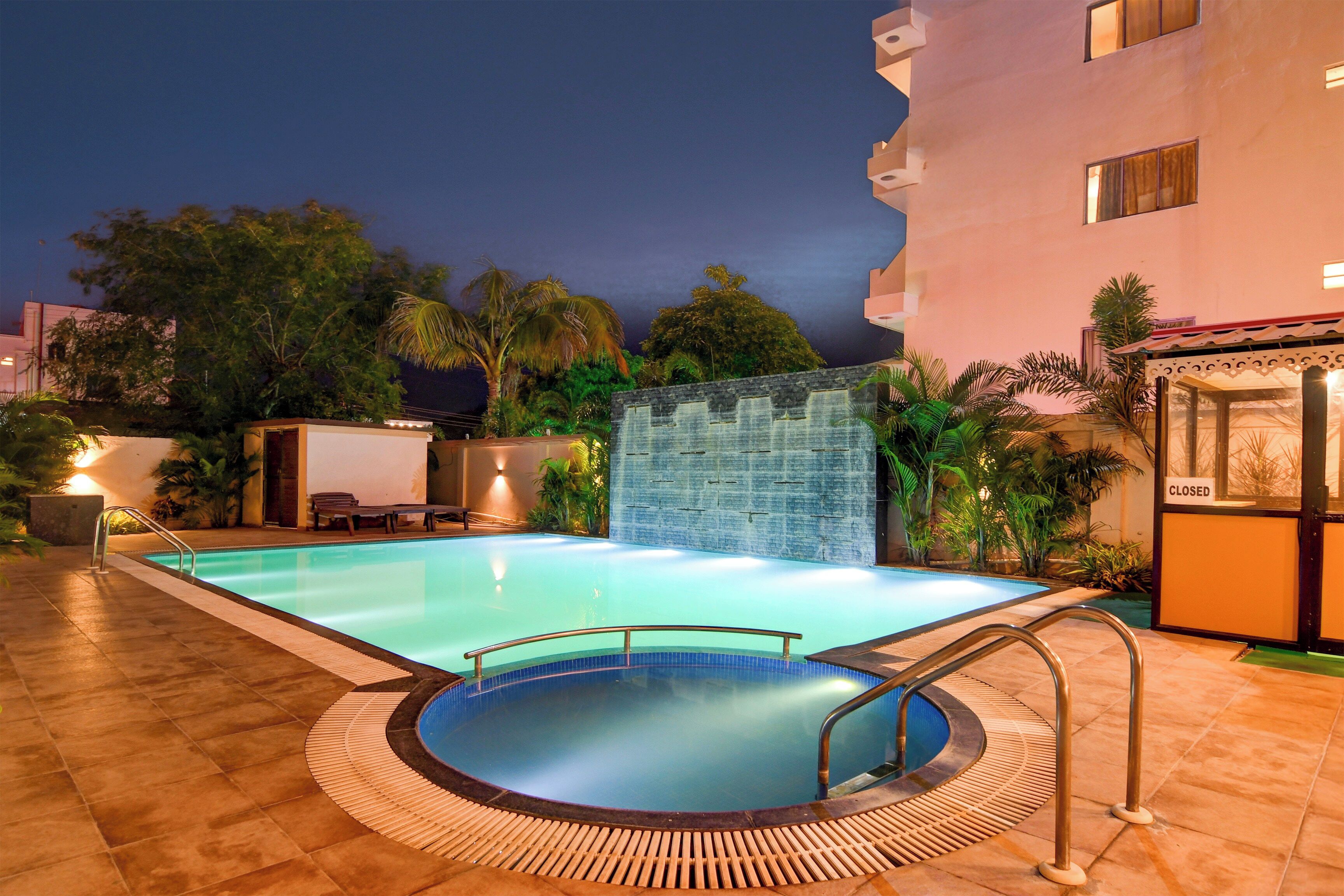 Une piscine avec une terrasse carrelée, un petit jacuzzi et un mur agrémenté d’un élément décoratif aquatique.