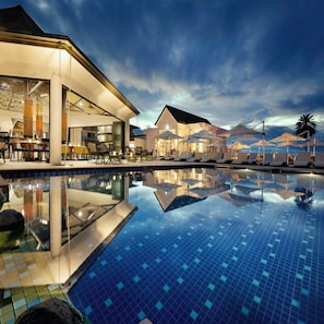 Een hotel met een zwembad, terras en parasols.