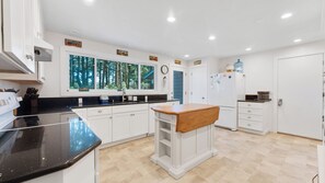 Une cuisine moderne avec des meubles blancs, un plan de travail noir et une fenêtre donnant sur une forêt.