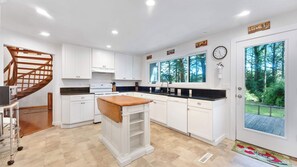 Una cocina moderna con armarios blancos, una isla de madera y vistas a un bosque a través de amplios ventanales.